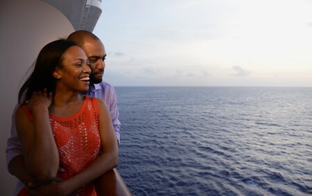A man and a woman embrace as they enjoy the ocean scenery from their verandah