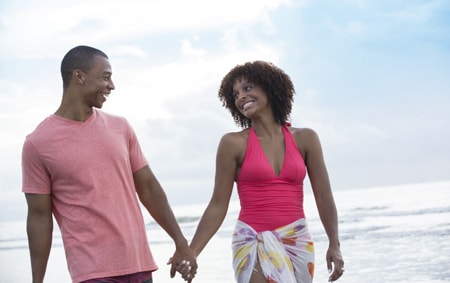 A man and a woman hold hands as they walk along the beach at Disney's Hilton Head Resort