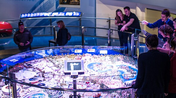 A group of people standing around a model display of a Disney park